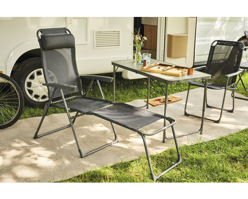 Scène avec une chaise longue, une chaise et une table devant une caravane.