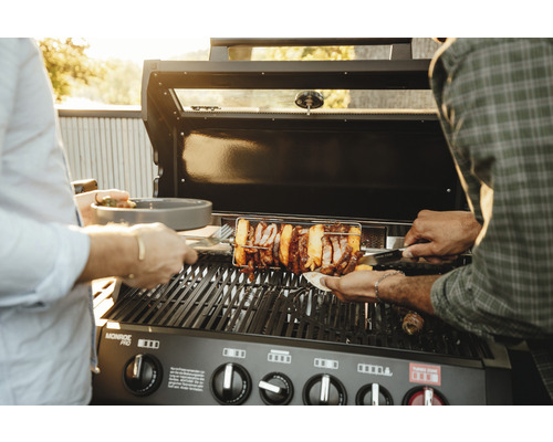 Barbecue à gaz avec tournebroche et personnes faisant griller des aliments.