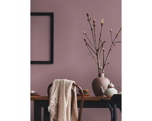 Salle à manger avec table en bois, vaisselle, vase avec des branches, couverture sur une chaise et un cadre noir au mur.