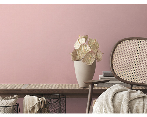 Intérieur clair avec des fleurs dans un vase et un fauteuil en rotin devant un mur rose