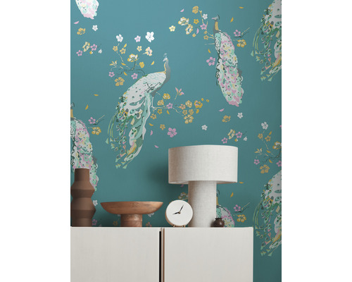 Wand mit Pfauen Tapetenmuster, dekoriert mit Lampe, Schale, Uhr und Vase auf einer Kommode.