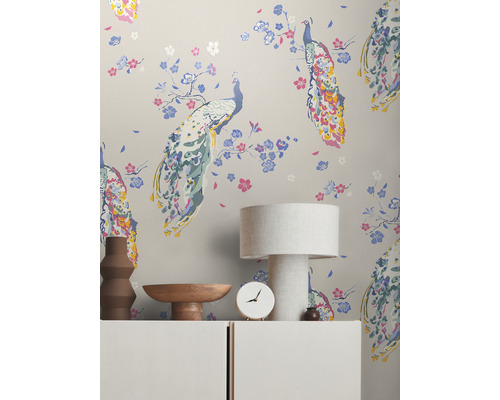 Szene mit Tapete mit Pfauenmuster, Tischleuchte, Uhr und Dekoration auf einem Schrank.
