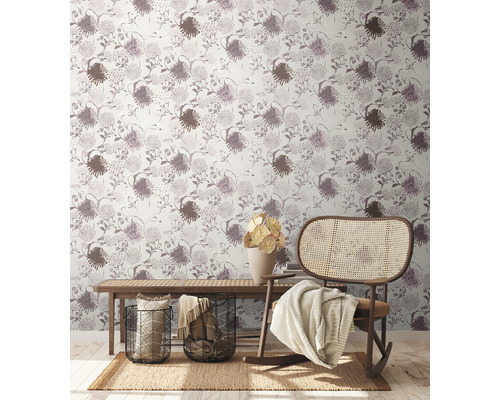 Coin salon confortable avec papier peint à fleurs, banc en bois, chaise en rotin, tapis et décorations.