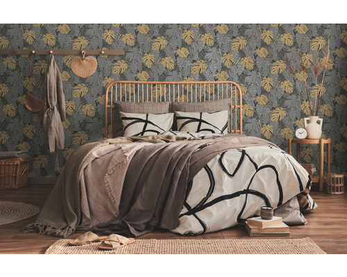 Schlafzimmer mit Bett vor einer gemusterten Tapete mit Pflanzenmotiven.