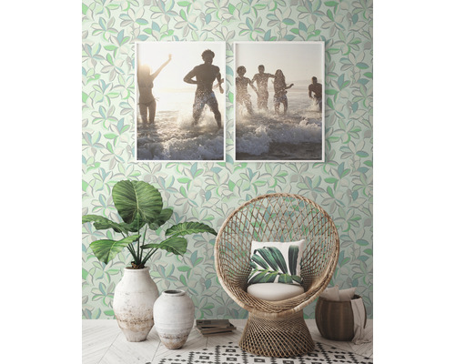 Pièce décorative avec papier peint à motifs, fauteuil en rotin, plantes et photos encadrées.