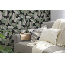 Salon décoratif avec canapé, coussins et papier peint mural à motif de feuilles.