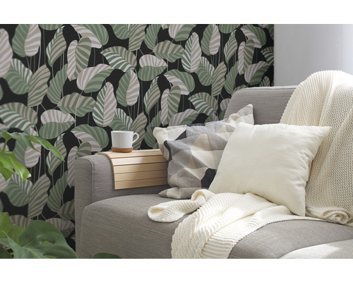 Salon décoratif avec canapé, coussins et papier peint mural à motif de feuilles.