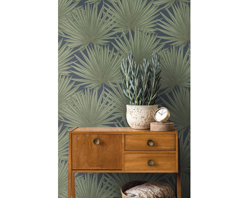Zimmeransicht mit botanischer Blättertapete, Holzkommode, Topfpflanze und Uhr.