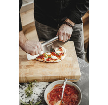 Une personne coupe une pizza sur une planche à découper en bois avec un coupe-pizza de la marque Enders.