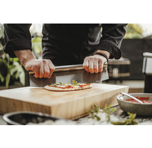 Une personne coupe une pizza avec un coupe-pâte sur une planche en bois.