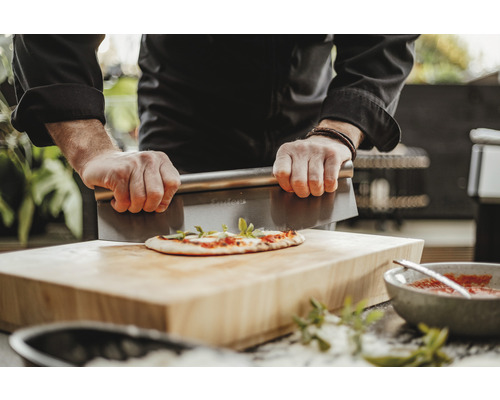 Une personne coupe une pizza avec un coupe-pâte sur une planche en bois.