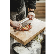 Une personne coupe une pizza sur une planche en bois avec un coupe-pizza.