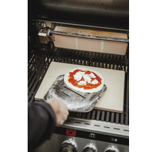 Pizza sur une pelle à pizza dans un barbecue avec une pierre à pizza