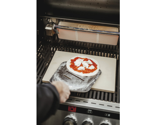 Pizza sur une pelle à pizza dans un barbecue avec une pierre à pizza