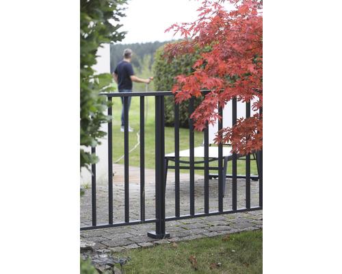 Aussenansicht eines Gartens mit Metallzaun und einer Person, die mit einem Gartenschlauch giesst