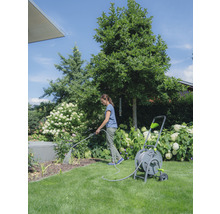 Frau bewässert Pflanzen mit einem Gartenschlauch auf einer Schlauchtrommel im Garten.