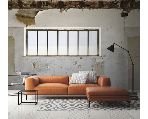 Salon avec canapé en cuir orange, ottoman, tapis et lampadaire devant une fenêtre