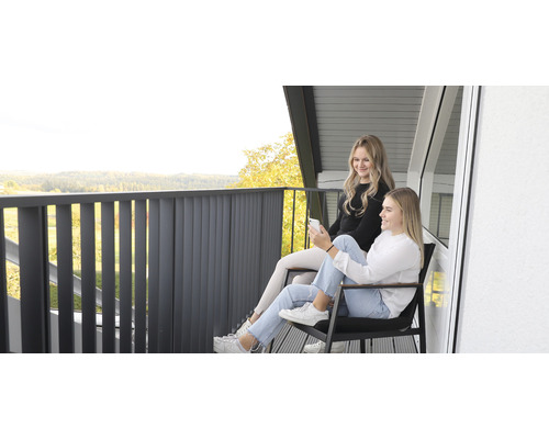 Zwei junge Frauen sitzen auf einem Balkon mit Metallgeländer und genießen die Aussicht.
