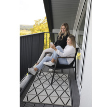 Deux femmes assises sur un balcon avec un tapis géométrique et une balustrade foncée.