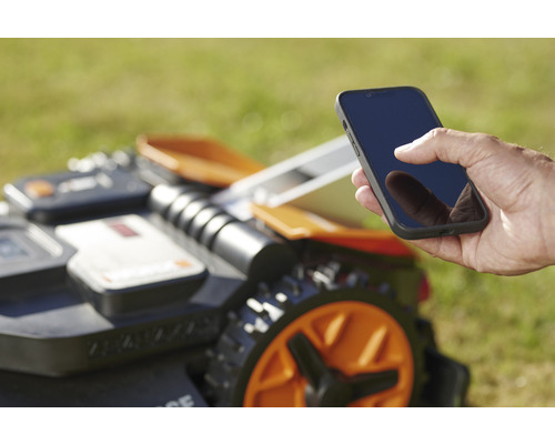 Un homme commande un robot de tonte avec un smartphone.