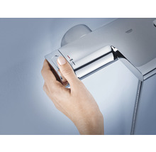 Une main règle la température sur une robinetterie de douche Grohe