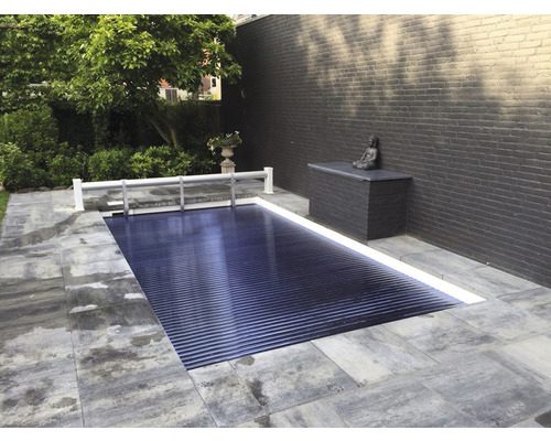 Außenaufnahme eines abgedeckten Swimmingpools im Garten mit Steinplatten und einer Mauer im Hintergrund.