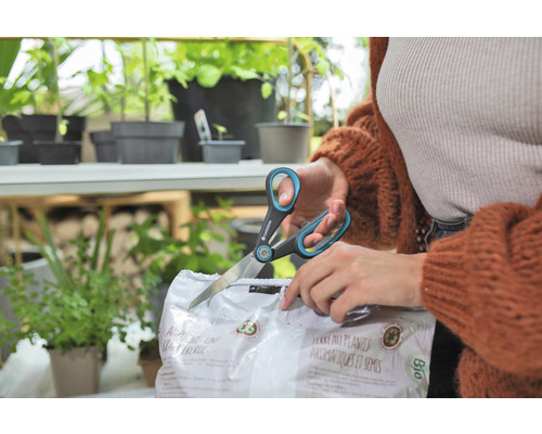 Une personne ouvre un paquet de terreau pour semis et herbes aromatiques avec des ciseaux de la marque Gardena.