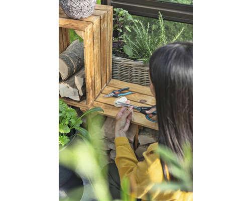 Frau schneidet Bindfaden mit einer Gartenschere neben Holzkisten und Pflanzen.