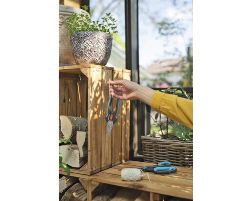 Szene im Garten mit Pflanzkasten, Holzscheiten, Gartenschere und einer Person