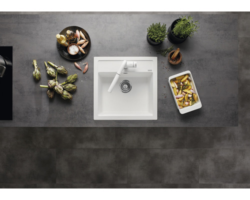 Küchenspüle mit Armatur, umgeben von Artischocken, Kräutern und zubereiteten Speisen auf einer Arbeitsplatte.