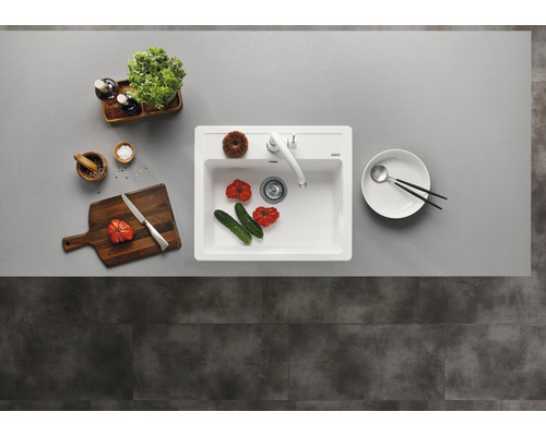 Ansicht von oben auf eine Spüle mit Armatur, Gemüse, Schneidebrett, Gewürzen und Geschirr auf einer Küchentheke