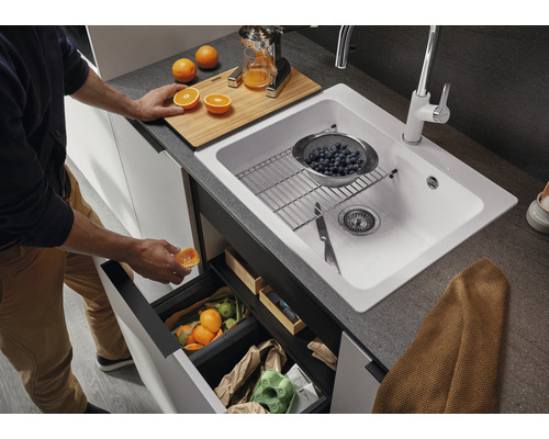 Scène de cuisine avec évier, robinet, poubelle et personne jetant une orange à la poubelle.