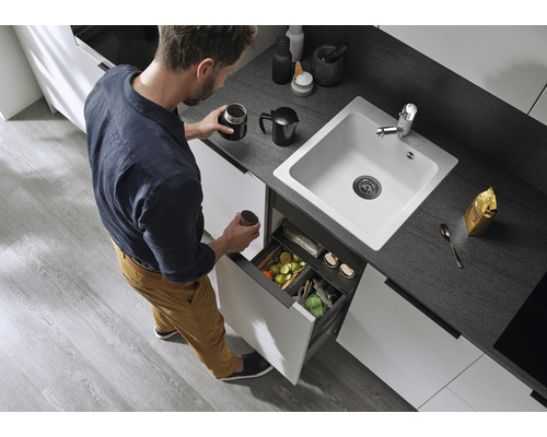 Ein Mann in einer Küche mit einer weißen Spüle und einem Abfalltrennsystem