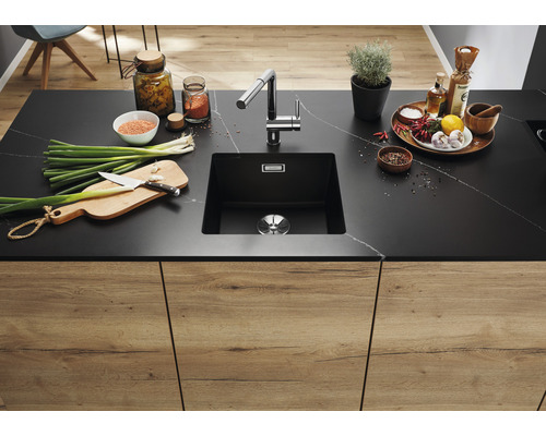 Küchenspüle aus schwarzem Material mit Armatur in einer modernen Küche mit Lebensmitteln auf der Arbeitsfläche