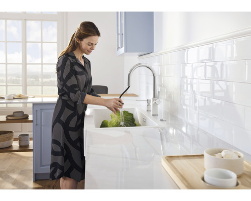 Femme lavant des légumes dans un évier avec robinet dans une cuisine lumineuse.