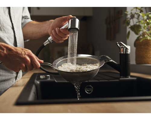 Une personne rince du riz avec un robinet de cuisine et une passoire au-dessus d''un évier.