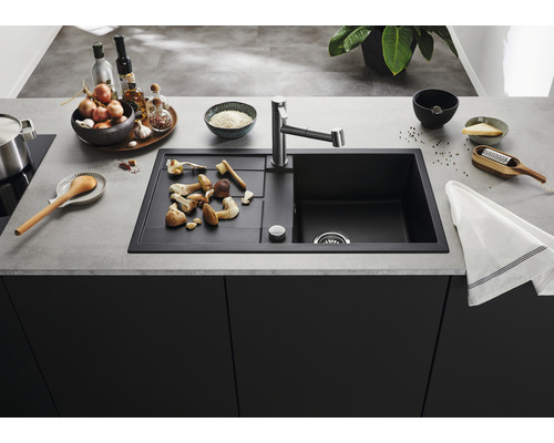 Évier de cuisine avec égouttoir, robinetterie et aliments sur le plan de travail.