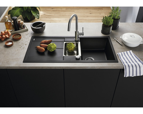 Spüle aus schwarzem Material mit Abtropffläche, Armatur und Gemüse