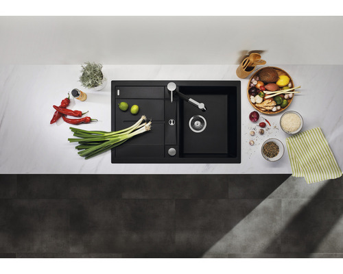 Schwarzes Spülbecken mit Abtropffläche und Armatur auf einer Küchentheke mit Gemüse