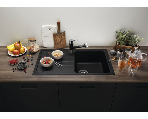 Schwarzes Spülbecken mit Armatur auf einer Küchentheke mit Frühstückszutaten und Geschirr