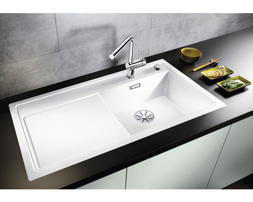 Weisses Spülbecken mit Abtropffläche und Wasserhahn auf einer dunklen Arbeitsplatte