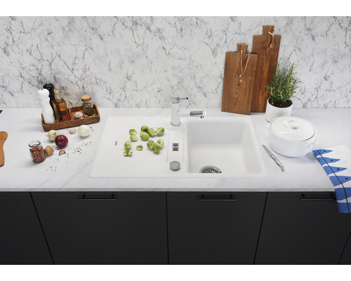 Évier de cuisine avec robinet, légumes et ustensiles de cuisine sur un plan de travail.