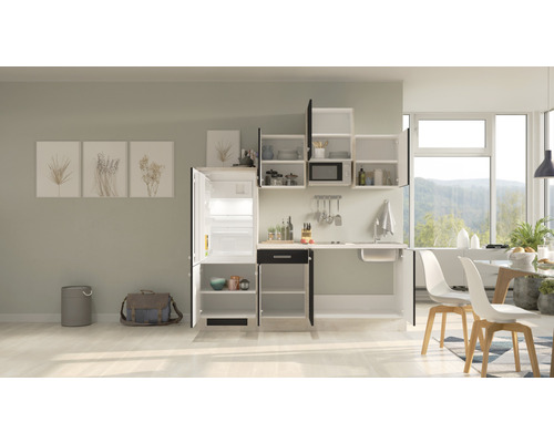 Cuisine compacte avec évier, réfrigérateur, armoires murales et table à manger dans une pièce lumineuse