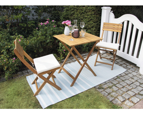 Scène de jardin avec table en bois, chaises et décoration sur un tapis rayé à l''extérieur.