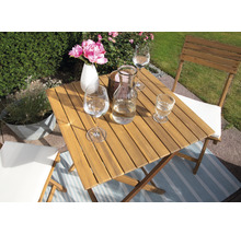 Table carrée en bois avec verres, fleurs et chaises dans le jardin.