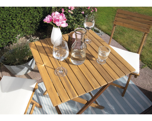 Table carrée en bois avec verres, fleurs et chaises dans le jardin.