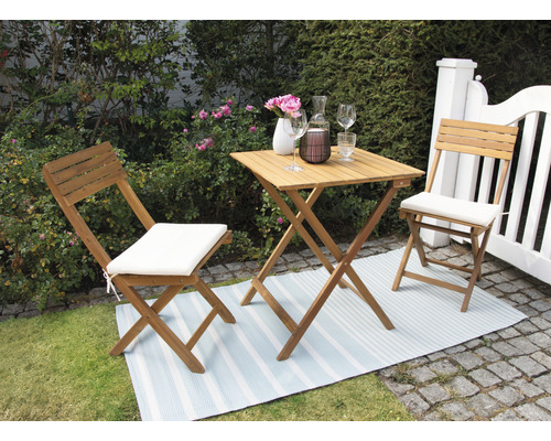 Scène de jardin avec table pliante et chaises pliantes avec coussins d''assise sur un tapis d''extérieur.