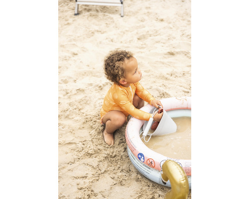Un enfant joue avec un seau et une pataugeoire sur la plage.
