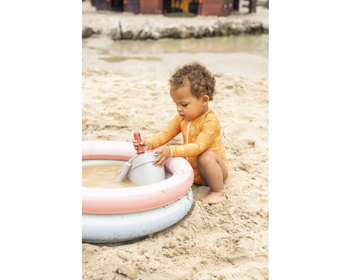 Un enfant joue avec des jouets de sable dans une piscine gonflable sur la plage.