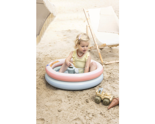 Une fille est assise dans une piscine gonflable pour enfants sur la plage, avec des jouets de sable à côté